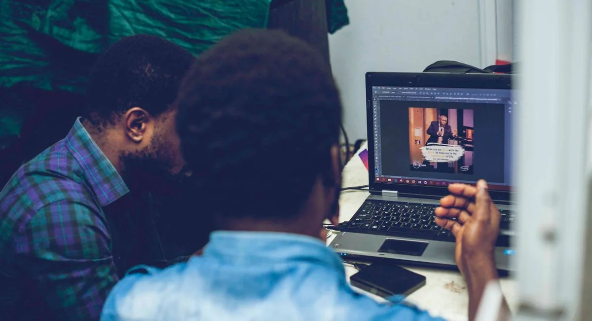 Two men collaborating on graphic design using a laptop indoors, focusing on technology and teamwork.